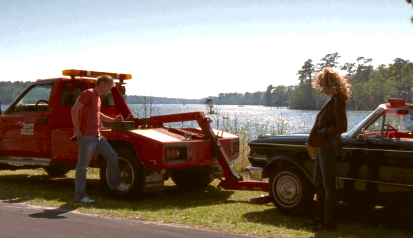 Two people standing next to a tow truck in front of a lake.