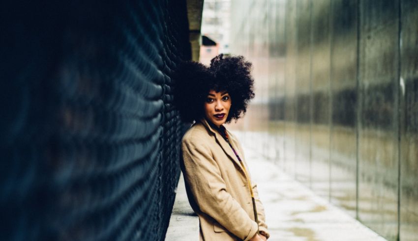 A woman with afro hair leaning against a wall.