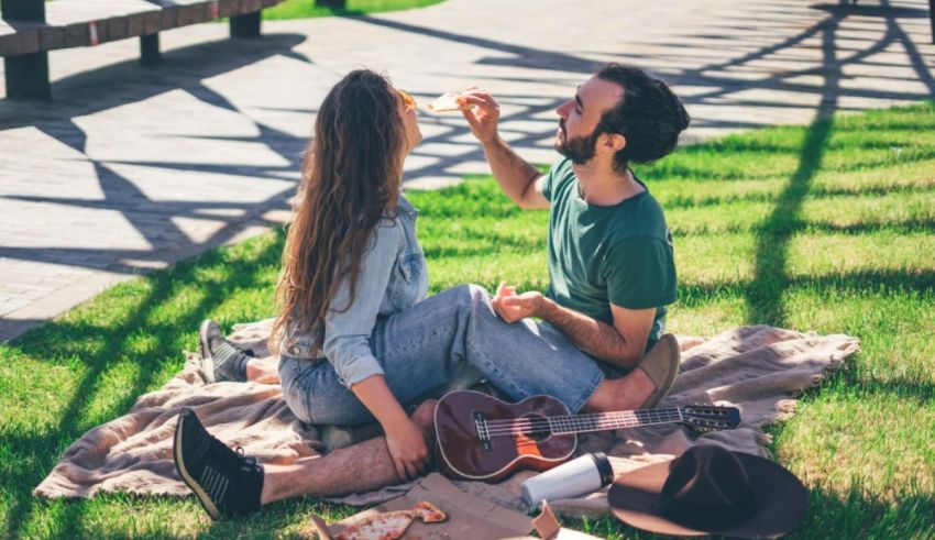 A man and woman sitting on a blanket eating pizza.