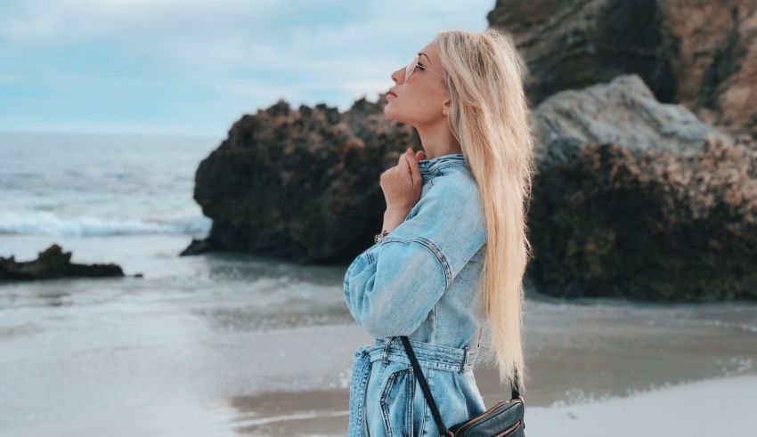 A blonde woman wearing a denim dress on the beach.