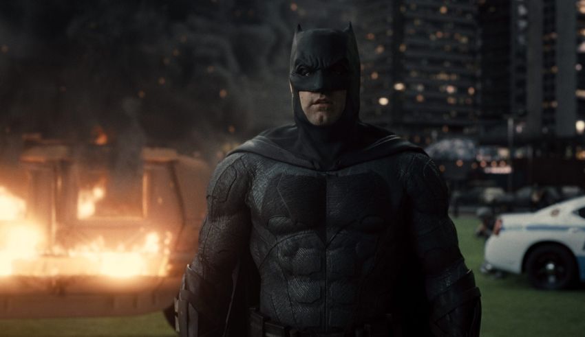 Batman is standing in front of a burning building.