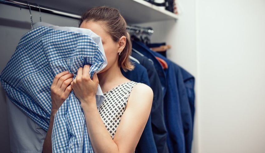 A woman is covering her face while looking at clothes in a closet.