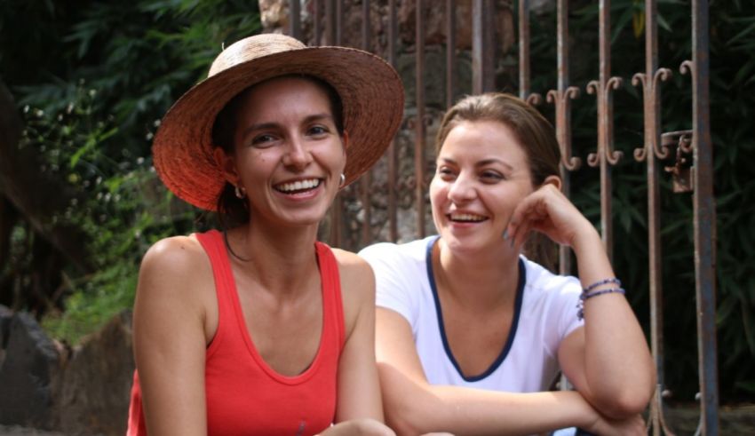 Two women smiling while sitting on a fence.