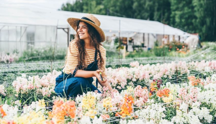 A woman in a hat and overalls sitting in a flower garden.