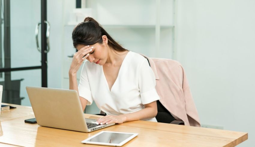 A woman sitting at a desk with her hand on her head.