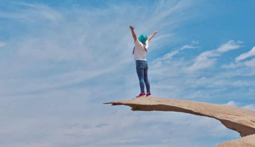 A woman standing on a rock with arms outstretched.