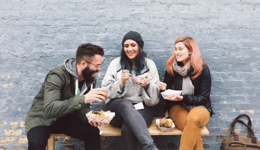 Three people sitting on a bench eating food.