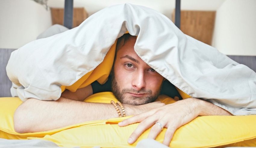 A man laying under a yellow blanket in bed.
