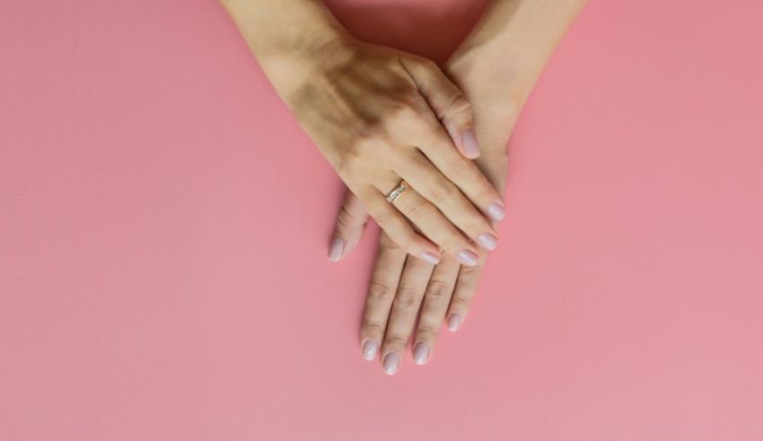 A woman's hands with a ring on a pink background.