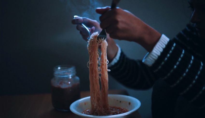 A person eating noodles with a spoon in the dark.