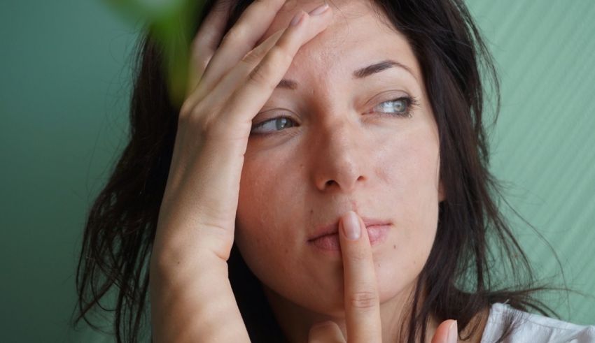 A woman is holding her finger to her face.