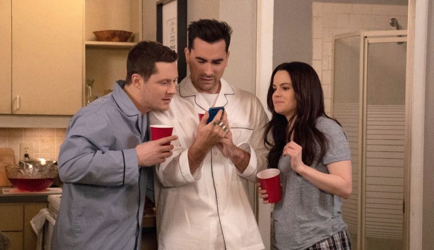 Three people looking at a cell phone in a kitchen.