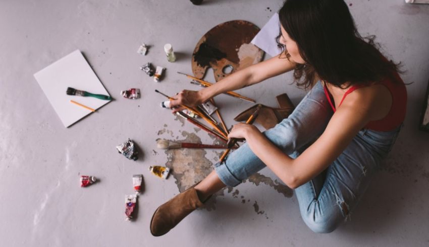 A woman sitting on the floor with paint brushes and paints.