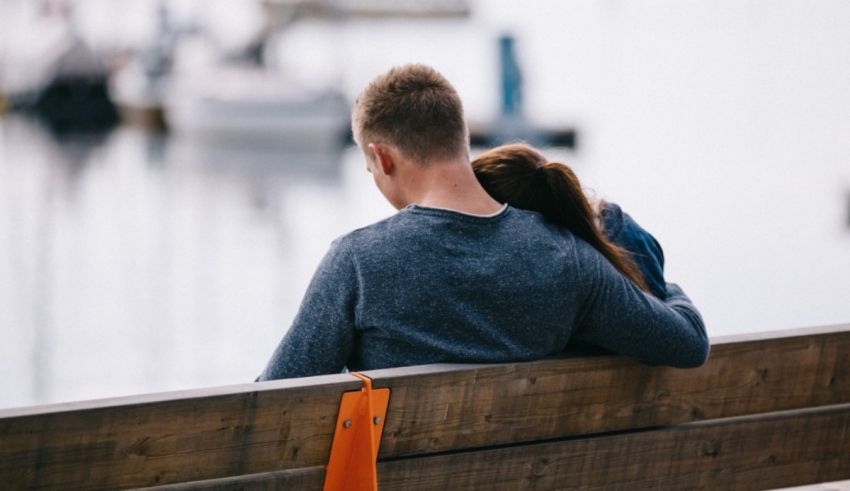 A man and woman sitting on a bench looking at the water.