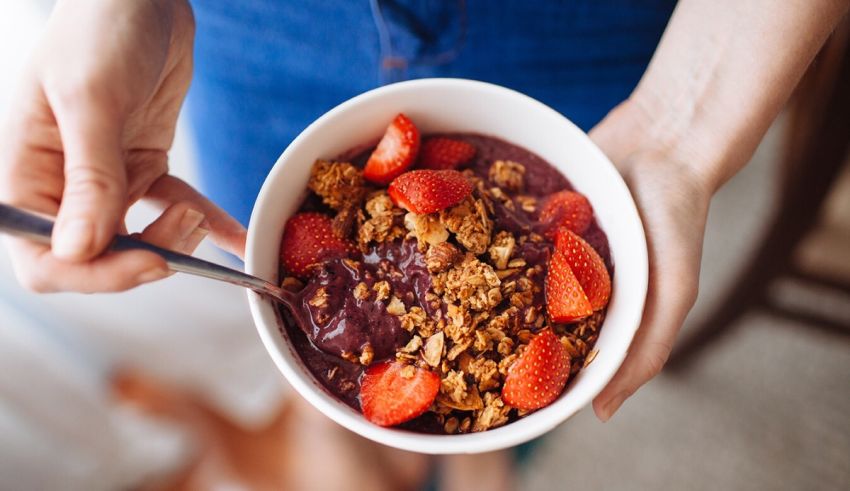 A woman holding a bowl of granola and strawberries.