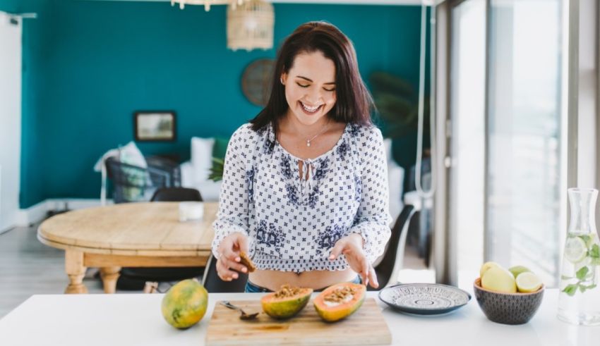 A woman smiling at a table with a cut papaya.