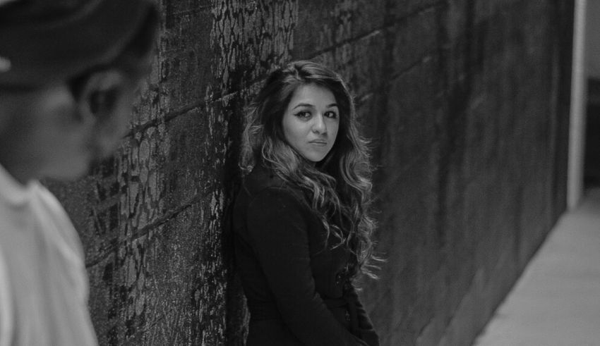 A black and white photo of a woman leaning against a wall.