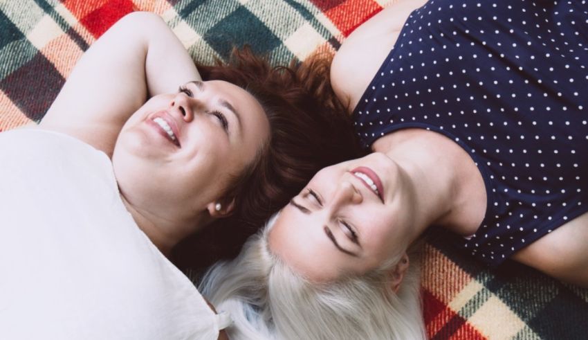 Two women laying on a blanket laughing.