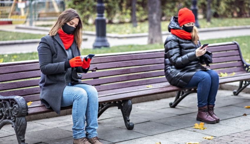 Two women sitting on a bench looking at their phones.
