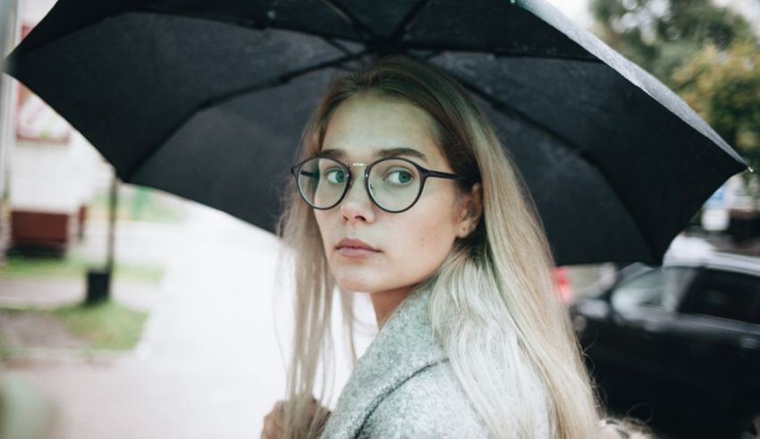A woman in glasses is holding an umbrella in the rain.
