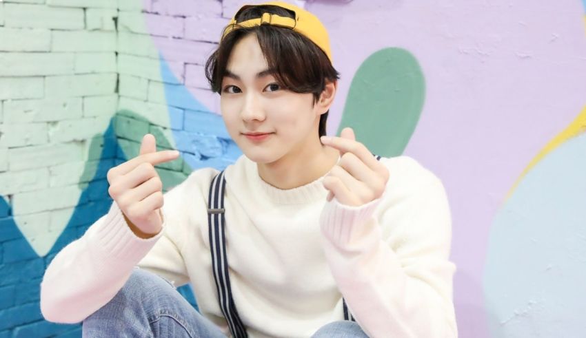 A young man with a hat and jeans sitting on a colorful wall.