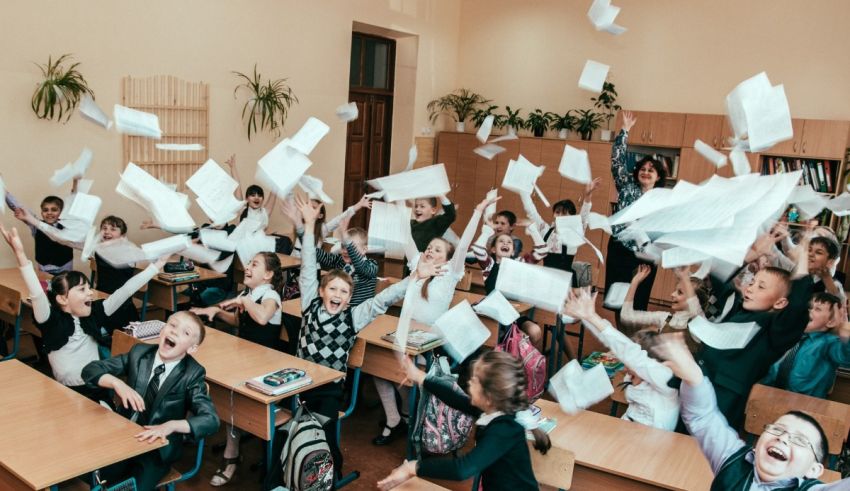 A group of children are throwing papers into the air in a classroom.