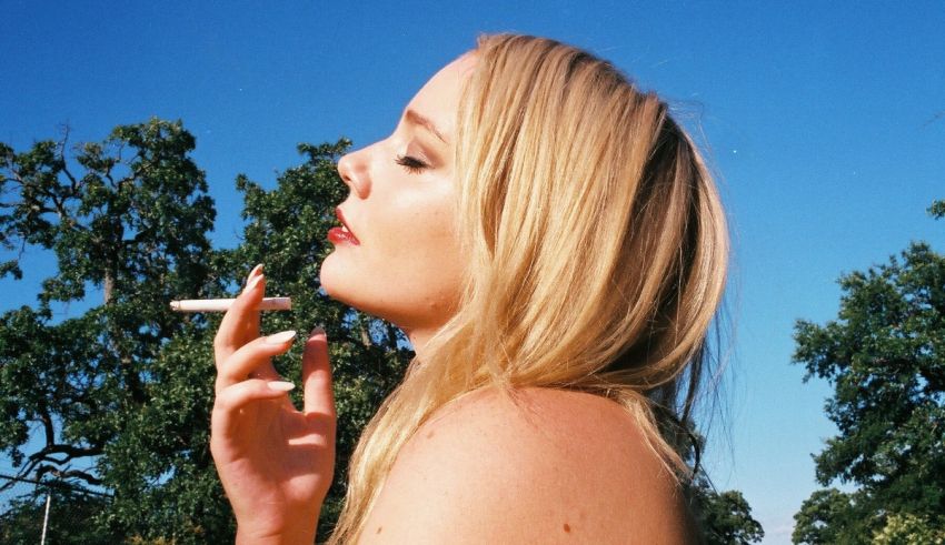 A blond woman smoking a cigarette in a field.