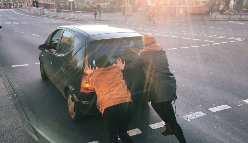 Two women pushing a car in the street.