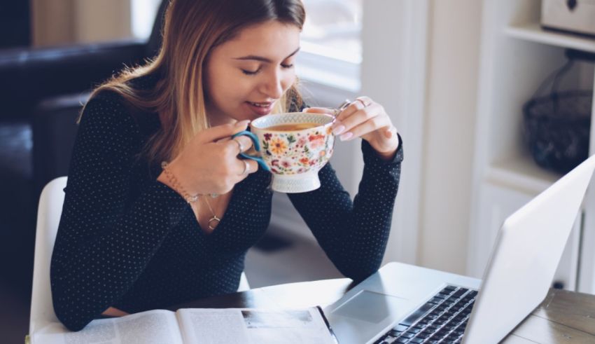 A woman drinking a cup of coffee while working on her laptop.