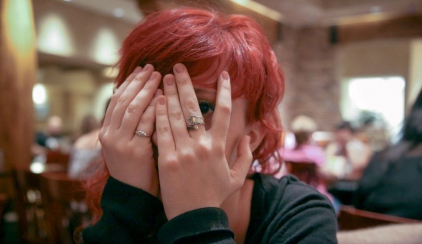 A woman with red hair covering her face with her hands.
