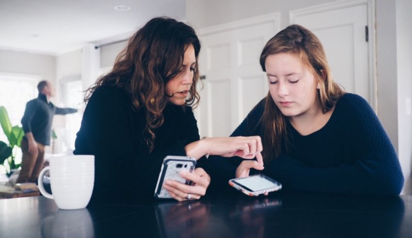 A mother and daughter looking at a cell phone while sitting at a table.