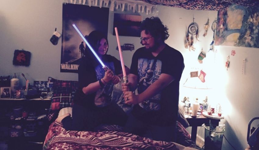 Two people holding lightsabers on a bed.