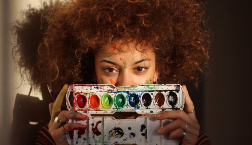 A woman holding a paint palette in front of her face.