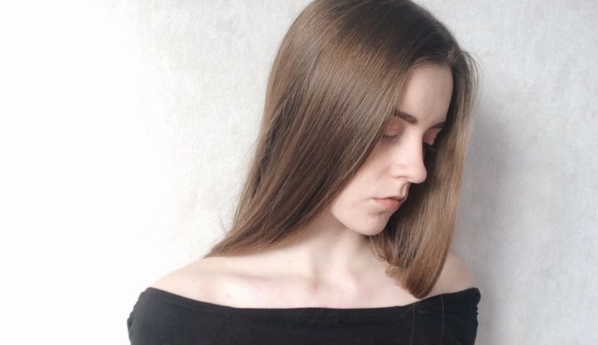 A woman with long brown hair is posing against a wall.