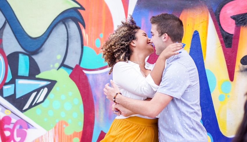 A couple kissing in front of a colorful wall.
