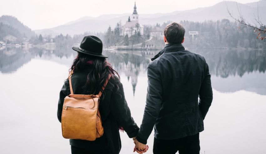 A couple holding hands in front of a lake with a castle in the background.