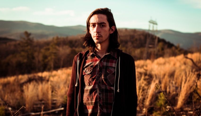 A young man in a plaid shirt standing in a field.