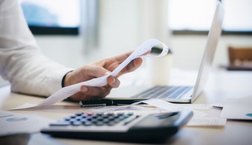 A person is holding a calculator and papers in front of a laptop.