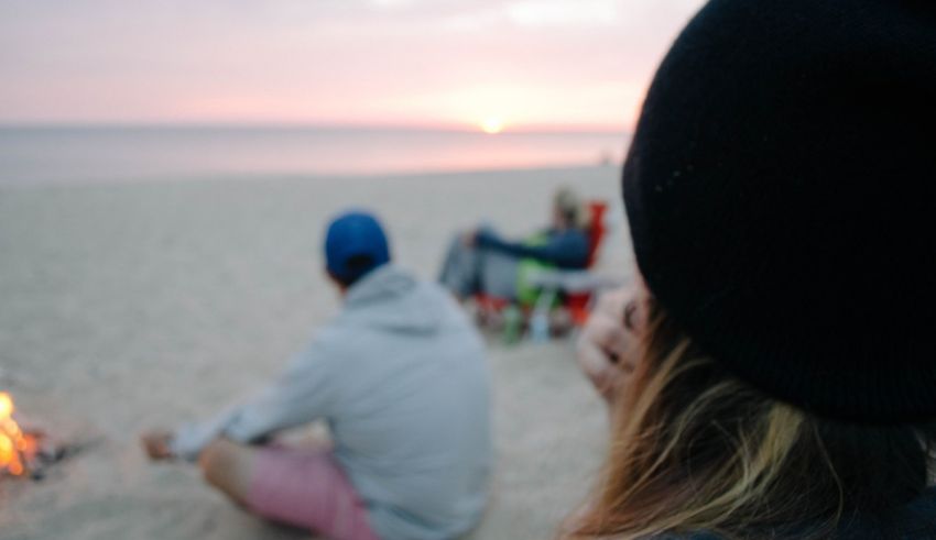 A group of people sitting around a campfire on the beach.