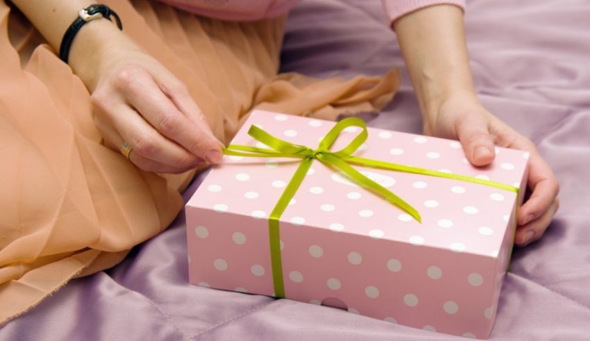 A woman is holding a pink gift box on a bed.