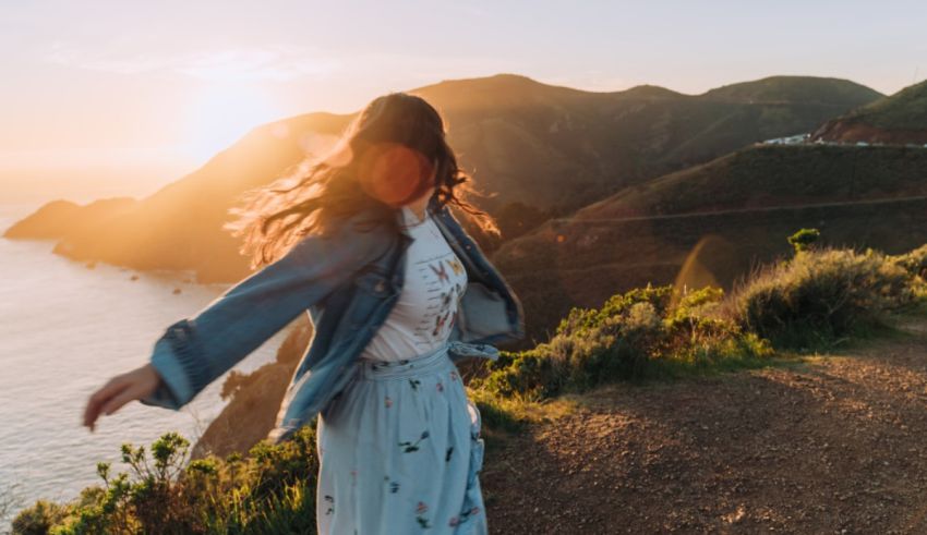 A woman is standing on a path near the ocean at sunset.