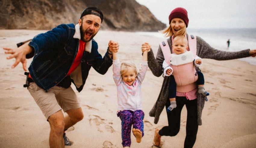 A family is running on the beach with a baby in a sling.