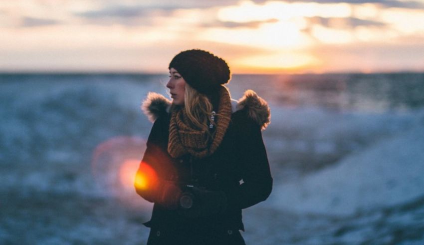 A woman is standing in the snow with a camera in her hand.