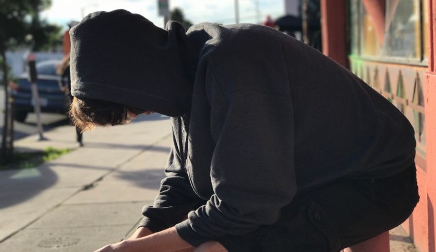 A man in a hoodie sitting on a sidewalk.