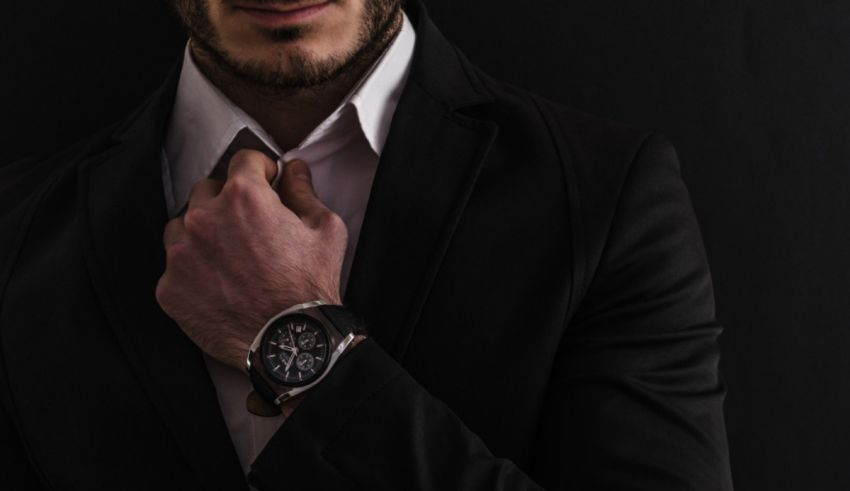 A man in a suit is adjusting his watch on a black background.