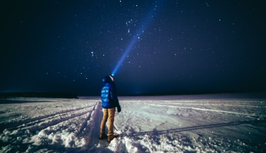 A man is standing in the snow looking at the stars.