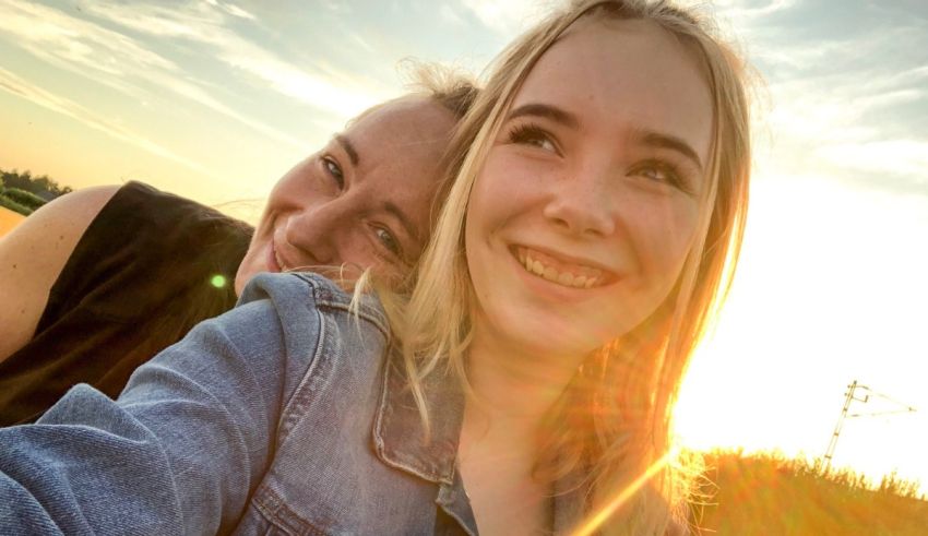 Two girls taking a selfie in a field at sunset.