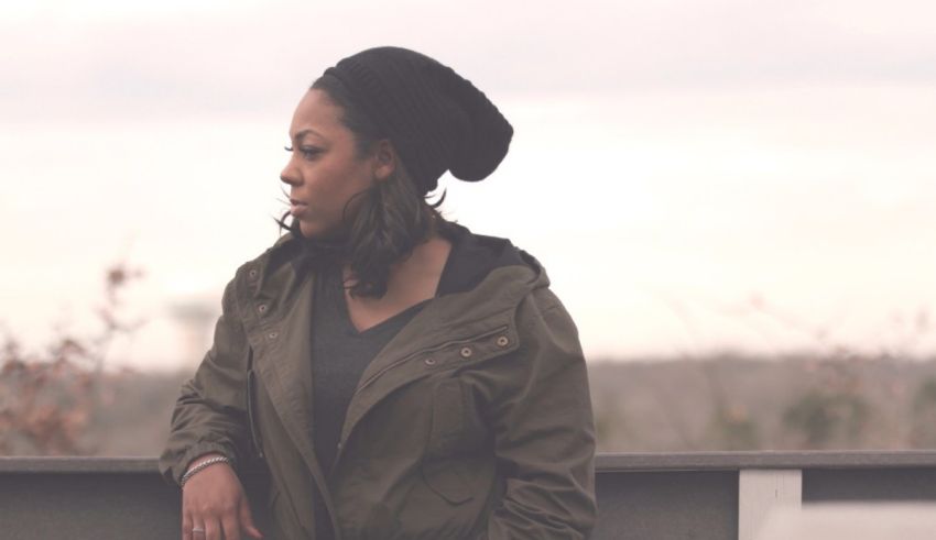 A woman wearing a jacket and hat is standing on a railing.