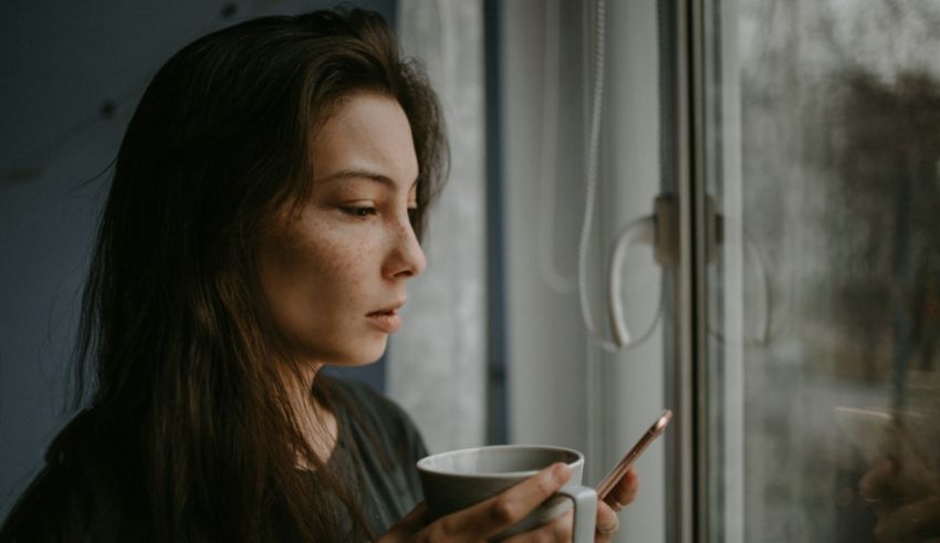 A woman looking out the window with a cup of coffee.