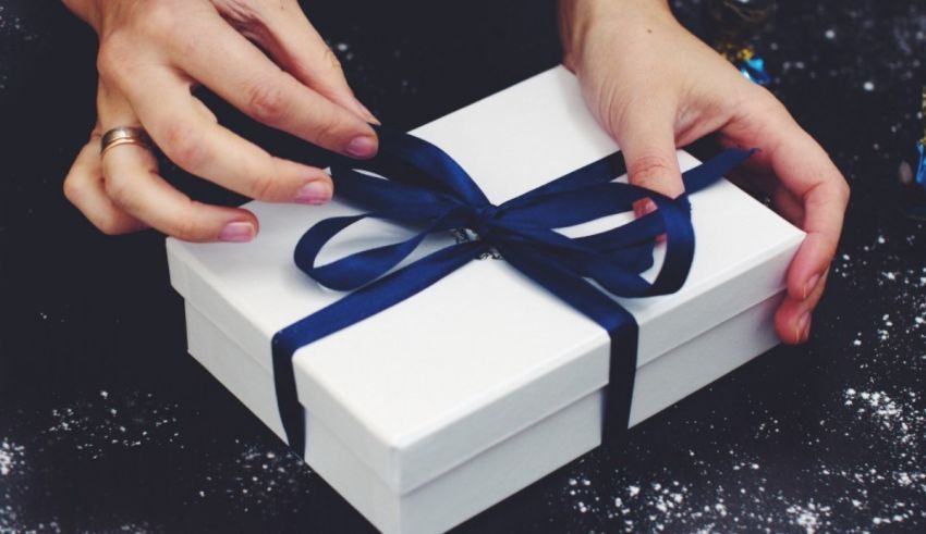 A woman is wrapping a gift in a white box with a blue ribbon.